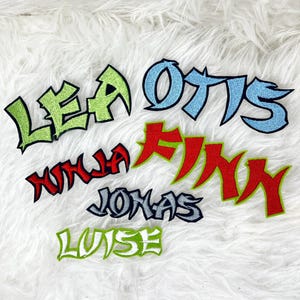 Könnte beinhalten: Ein Set bunter Bügelbilder mit Namen, die im Graffiti-Stil geschrieben sind. Die Namen sind Lea, Otis, Ninja, Finn, Jonas und Luise.