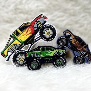 Könnte beinhalten: Drei Monstertruck-Patches, einer gelb und rot, einer grün und einer braun, mit schwarzen Rädern. Die Patches sind gestickt und haben ein detailliertes Design.