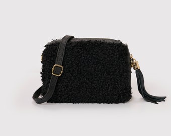 Könnte beinhalten: Eine schwarze Umhängetasche aus Kunstfell mit einer goldenen Schnalle und einem schwarzen Quastenanhänger.
