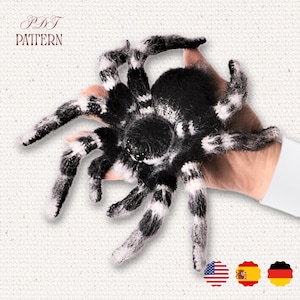 Puede incluir: Una araña de peluche en blanco y negro con largas patas segmentadas. La araña se sostiene en una mano, mostrando su diseño detallado. La imagen incluye el texto "PDF PATTERN" en la parte superior.