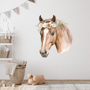 May include: A watercolour illustration of a horse's head, with a brown coat and a white stripe on its face. The horse is adorned with a floral crown of beige and green flowers. This wall decal is suitable for a nursery or children's room.