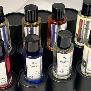 May include: A collection of eight glass bottles of perfume with black lids and labels. The labels feature the text "B.C. Parfums" and the names of different fragrances, including "Tom Ford Last Cherry", "Creed Virgin Island Water", and "Tom Ford Oud Leather".