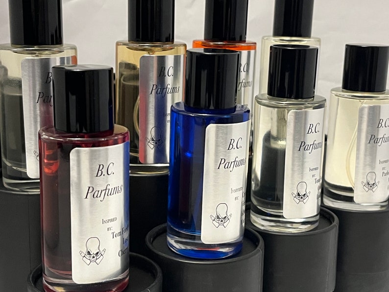 May include: A collection of eight small glass bottles with black caps and silver labels. The labels feature the text "B.C. Parfums" and a skull graphic. The bottles are filled with different colored liquids.