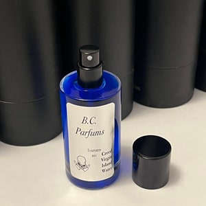 May include: A blue glass bottle of perfume with a black spray nozzle and cap. The bottle has a white label with the text "B.C. Parfums" and "Inspired by: Creed Virgin Island Water".