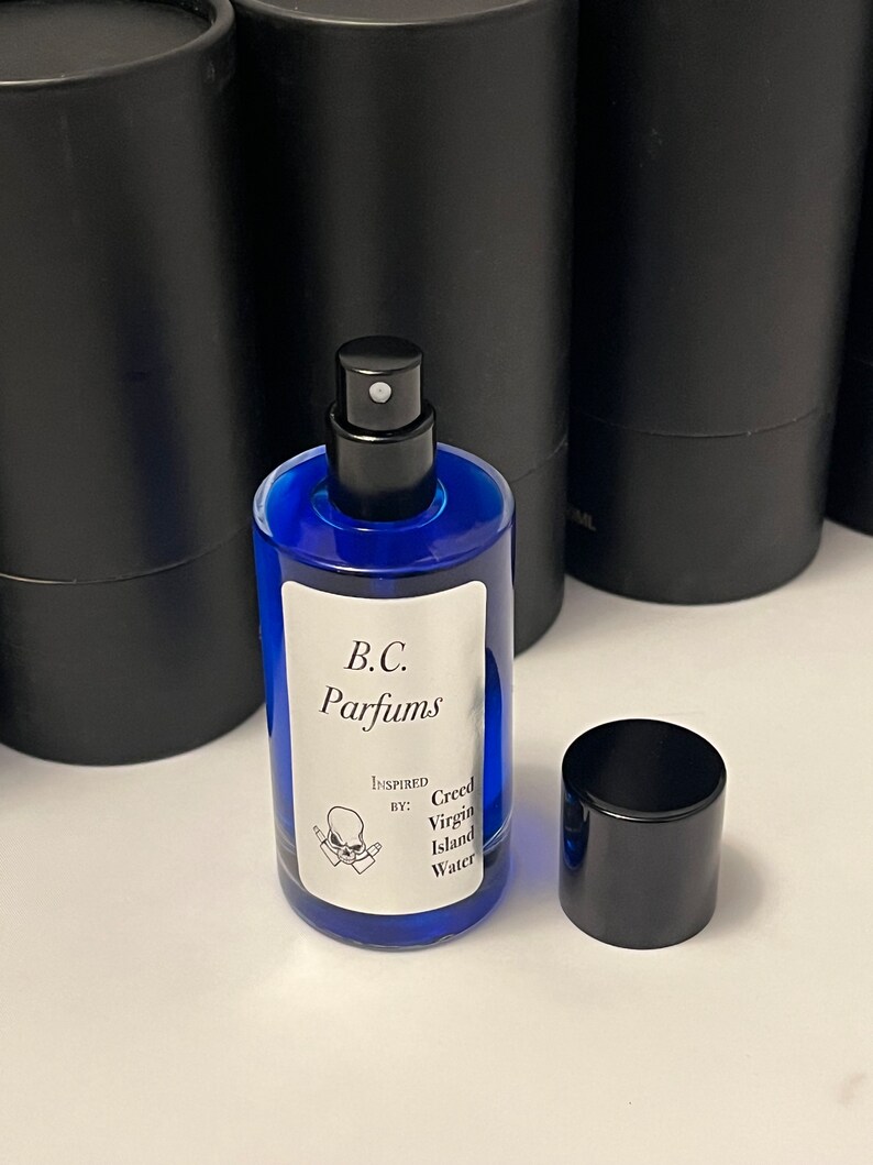 May include: A blue glass bottle of perfume with a black spray nozzle and cap. The bottle has a white label with the text "B.C. Parfums" and "Inspired by: Creed Virgin Island Water".