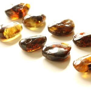 May include: A collection of amber stones in various shades of brown and yellow. The stones are smooth and polished, and they have a natural, organic look.