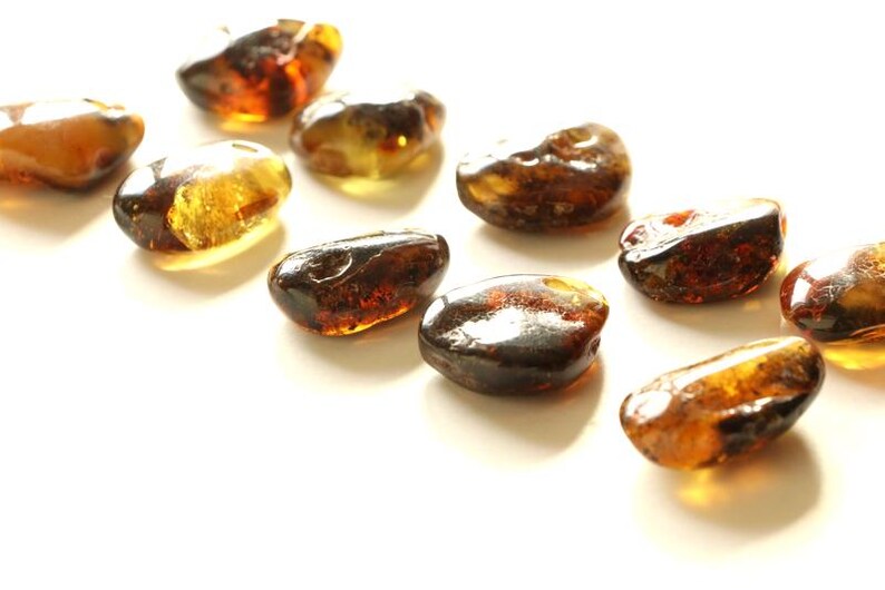 May include: A collection of amber stones in various shades of brown and yellow. The stones are smooth and polished, and they have a natural, organic look.