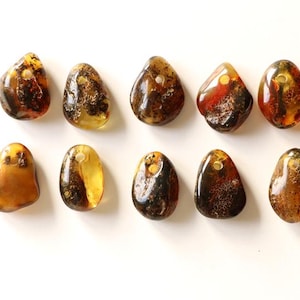 May include: Ten amber stone pendants with a hole drilled through the top. The stones are various shades of brown, yellow, and orange, and have a natural, irregular shape.