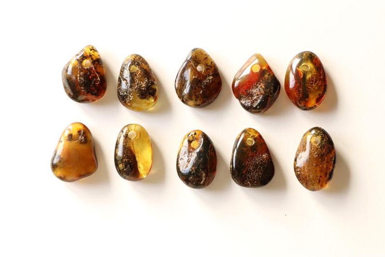 May include: Ten amber stone pendants with a hole drilled through the top. The stones are various shades of brown, yellow, and orange, and have a natural, irregular shape.