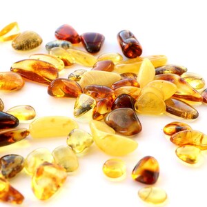 May include: A collection of amber stones in various shades of yellow, orange, and brown. The stones are smooth and polished, and they are scattered on a white background.