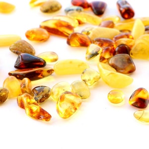 May include: A collection of amber stones in various shades of yellow, orange, and brown. The stones are scattered on a white background.