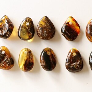 May include: Ten amber stone pendants with a hole for stringing. The stones are various shades of brown and yellow, with some having inclusions.