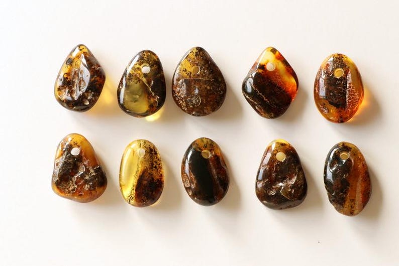 May include: Ten amber stone pendants with a hole for stringing. The stones are various shades of brown and yellow, with some having inclusions.