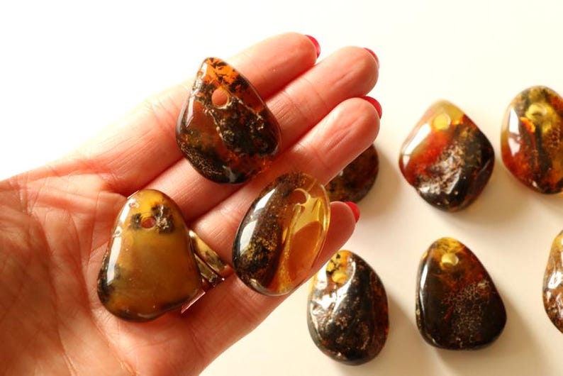May include: A collection of seven amber gemstone pendants, each with a unique shape and color variation. The pendants are a mix of brown, orange, and yellow hues, with some featuring inclusions of natural materials.