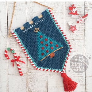 Puede incluir: Un tapiz de pared de árbol de Navidad de color azul teal tejido a crochet con ribetes rojos y blancos. El árbol está decorado con estrellas rojas y doradas. El tapiz tiene una varilla de madera en la parte superior y una borla roja en la parte inferior. El texto "@CHICA.OUTLET" está en el tapiz.