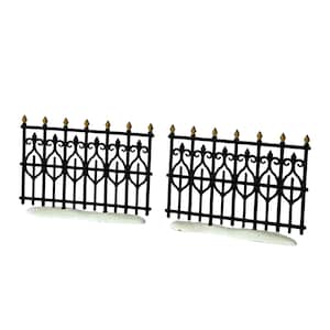 May include: Two black miniature fence sections featuring a decorative metal-style pattern with pointed finials tipped in gold. Each fence segment is mounted on a white, snow-textured base, creating a winter-themed display piece for dioramas.