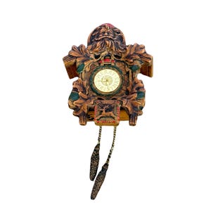 May include: A vintage wooden cuckoo clock with a Christmas theme. The clock features a Santa Claus design at the top, with a gold-colored clock face that reads "Merry Christmas". The clock has decorative leaves and two hanging weights.