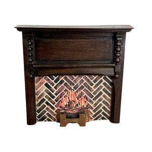 May include: A miniature wooden fireplace in dark brown. It has a brick-patterned interior and a depiction of flames. The mantelpiece has decorative detailing. A small, gold-coloured stand holds the flames.
