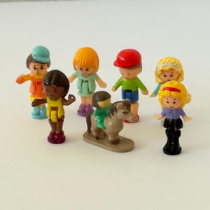 Pode incluir: Uma coleção de pequenas figuras de brinquedo de plástico, incluindo crianças e um cavalo. As figuras são de várias cores, algumas usando chapéus e roupas diferentes. O cavalo tem uma sela verde. Os brinquedos estão em uma superfície branca.