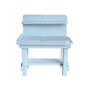 May include: A small, light blue wooden desk with a distressed, crackled finish. The desk has a shelf, a raised back, and a lower shelf. The legs are square and the overall design is simple and functional.