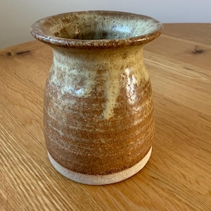 May include: A handmade ceramic vase with a wide, slightly flared rim. The vase has a speckled brown and tan glaze, with a lighter interior. The base is a natural, unglazed colour. This decorative vase is suitable for displaying flowers or as a standalone art piece.
