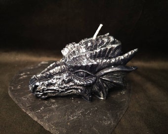 May include: A black dragon head candle with silver detailing. The candle is on a black slate surface.