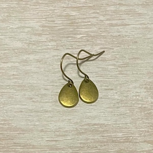 May include: A pair of small, teardrop-shaped earrings. The earrings are a muted gold color and hang from curved ear wires. The earrings are simple and elegant, suitable for everyday wear.