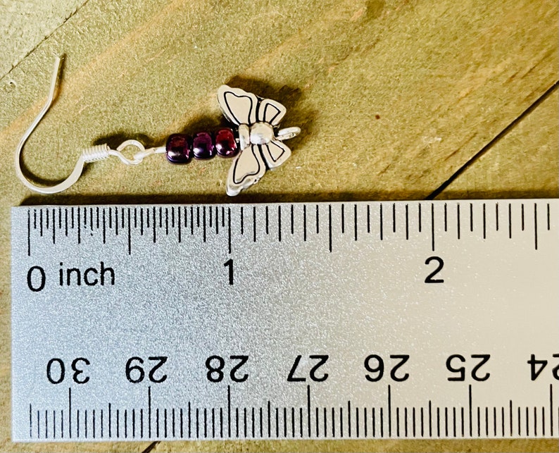 May include: Silver butterfly dangle earrings with purple beads. The earrings measure approximately 1 inch in length.