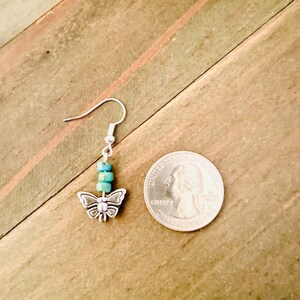 May include: Silver butterfly dangle earrings with turquoise blue beads. The earrings are shown next to a US quarter for size reference.