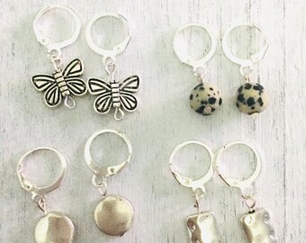 May include: Six pairs of silver knitting stitch markers with different charms. Two pairs feature butterfly charms, two pairs feature round stone charms, and two pairs feature square stone charms.