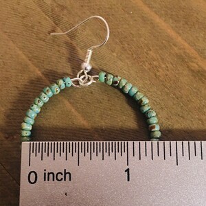 May include: A pair of turquoise beaded hoop earrings with silver hooks. The earrings are approximately 1 inch in diameter.