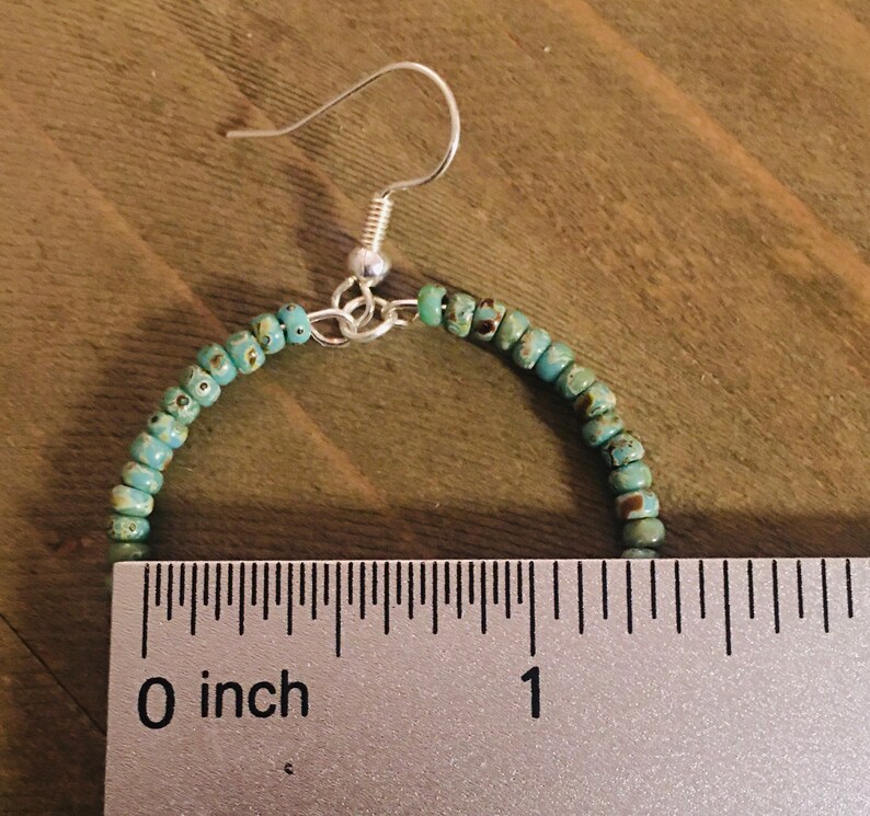 May include: A pair of turquoise beaded hoop earrings with silver hooks. The earrings are approximately 1 inch in diameter.