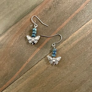 May include: A pair of silver butterfly earrings with blue and white speckled beads hanging from the bottom.