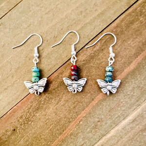 May include: Three pairs of silver butterfly earrings with colorful stone beads. The earrings have a silver butterfly charm at the bottom and a silver hook closure.