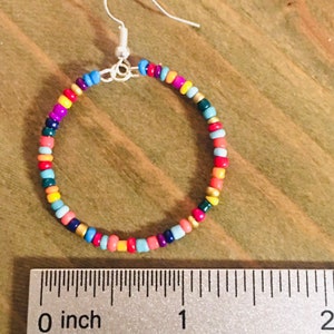 May include: A pair of colorful beaded hoop earrings with a silver hook closure. The earrings are approximately 1 inch in diameter and feature a variety of colors, including red, orange, yellow, green, blue, and purple.