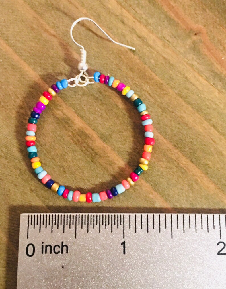 May include: A pair of colorful beaded hoop earrings with a silver hook closure. The earrings are approximately 1 inch in diameter and feature a variety of colors, including red, orange, yellow, green, blue, and purple.