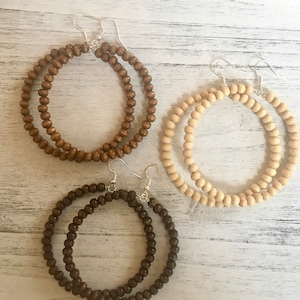 May include: Three pairs of large hoop earrings made of wooden beads. The earrings are in three different colors: brown, light brown, and natural wood.