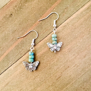 May include: A pair of silver butterfly earrings with turquoise blue beads.