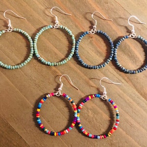 May include: Four pairs of hoop earrings made with small beads. The earrings are in four different color combinations: teal, blue, multi-colored, and multi-colored.