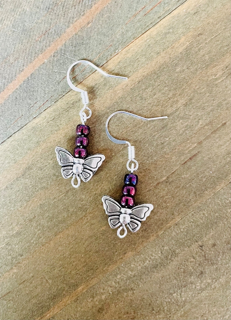 May include: A pair of silver butterfly earrings with purple and pink iridescent beads hanging from the bottom.
