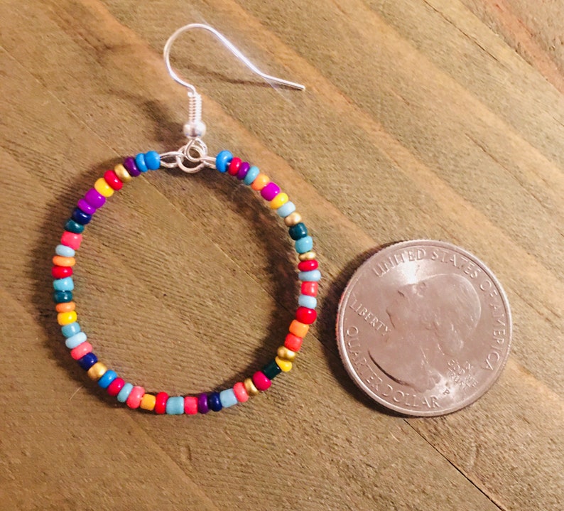 May include: Colorful beaded hoop earrings with a silver hook closure. The earrings are about the size of a US quarter.
