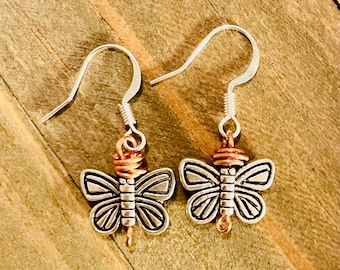 May include: A pair of silver butterfly earrings with copper wire accents. The butterflies have a detailed design and are attached to silver hooks.