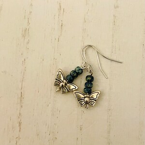May include: A pair of silver butterfly earrings with blue and green speckled beads hanging from the bottom.