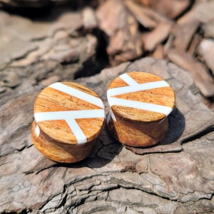 May include: Two wooden ear gauges with a white geometric pattern. The gauges are brown with white lines.