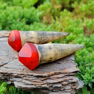 May include: A pair of wooden ear gauges with red resin tips. The gauges are tapered and have a natural wood finish.