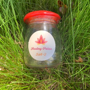 May include: A clear glass jar with a red lid and a white label that says "Healing Potion 2d4+2". The jar is sitting in a bed of green grass.