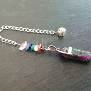 May include: A silver chain with a small ball at the end, attached to a crystal pendulum with a silver setting. The pendulum is a green and pink crystal with a pointed tip. The chain has a rainbow of small crystals attached to it.