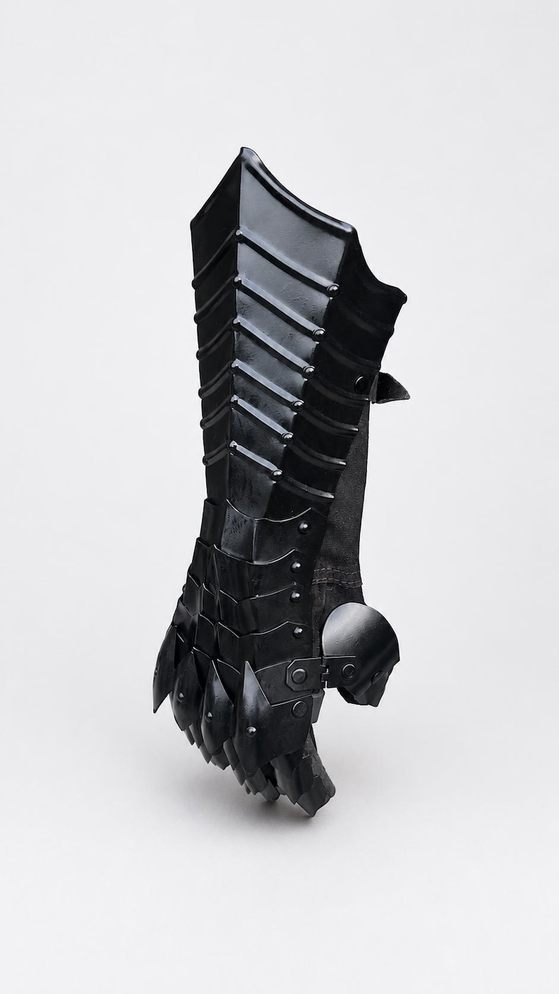 K&ouml;nnte beinhalten: Ein schwarzer, beweglicher Panzerhandschuh mit geschichteten Metallplatten, die Unterarm und Hand bedecken. Das Design umfasst eine Reihe &uuml;berlappender Segmente, die mit Nieten befestigt sind und vom Handgelenk bis zu den Kn&ouml;cheln reichen.