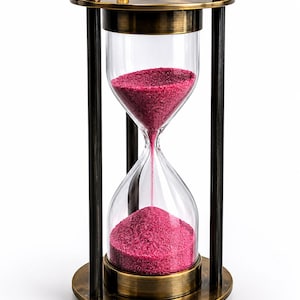 May include: An hourglass featuring a clear glass bulb filled with vibrant magenta sand. The frame is constructed from antique-finished brass with a circular base and top, supported by three vertical pillars. The design includes small decorative spheres.