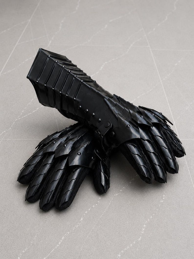 K&ouml;nnte beinhalten: Ein Paar schwarze, bewegliche Panzerhandschuhe mit &uuml;berlappenden Metallplatten, die die Finger und den Handr&uuml;cken bedecken, verbunden mit einer starren, segmentierten Manschette, die den Unterarm bedeckt und mit Nieten befestigt ist.